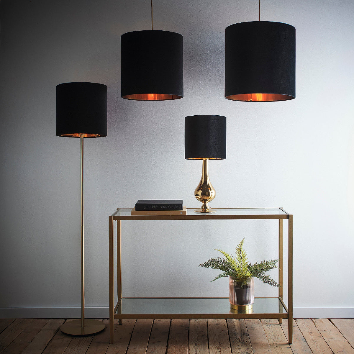 A styled interior scene with three black drum pendant lamps and a matching floor lamp, plus a small table lamp, set against a light gray wall and wood floor.