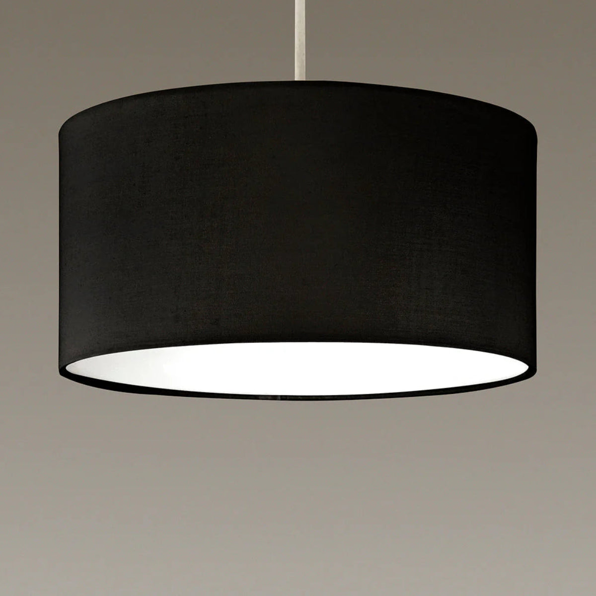 A black fabric drum pendant light hanging from a thin silver cord against a neutral gray background.