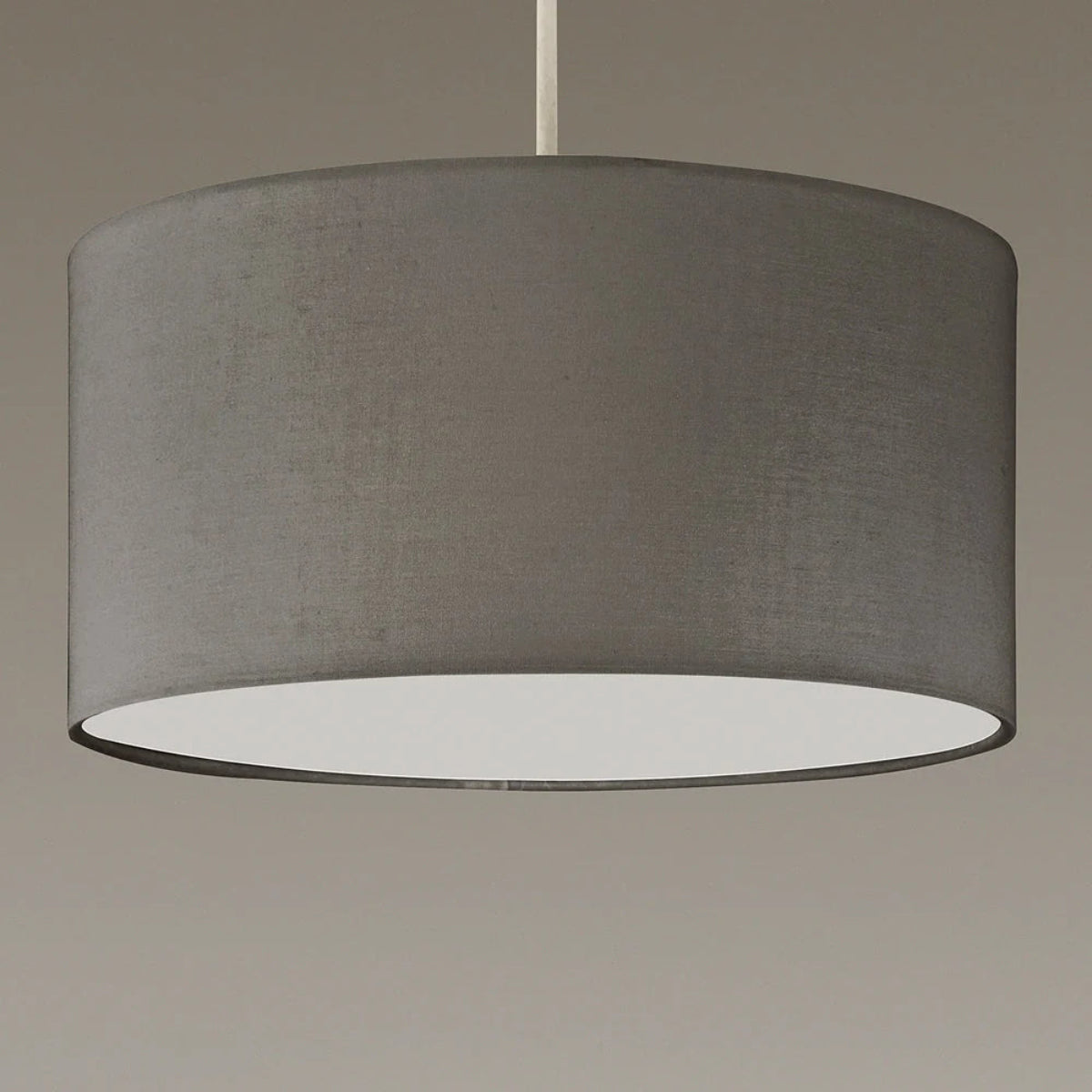 A large drum pendant light shade made of textured gray fabric, suspended by a slim white rod against a neutral gray background.